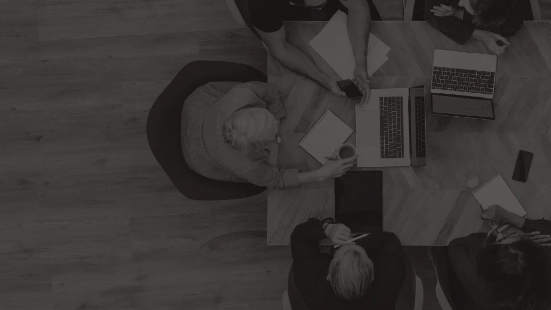 A group of workers are sat at a boardroom table working and conversing.