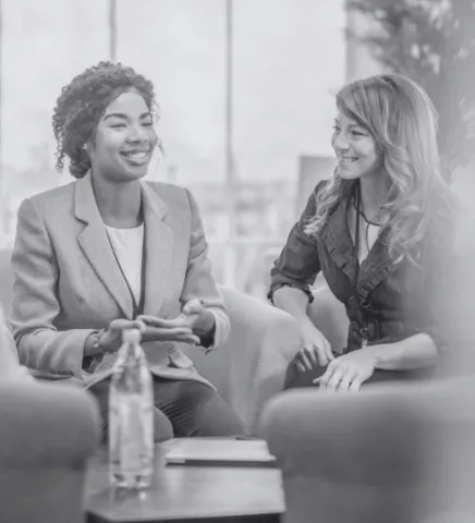 Two women are sat in a boardroom conversing.