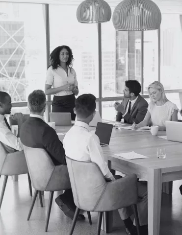 Welcome to CharityVillage eLearning | A woman stands at the front of a boardroom table presenting to a group of colleagues.