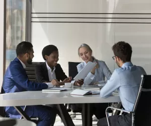 Four individuals are sat at a boardroom table conversing.
