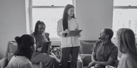 A woman is stood presenting to a group of people in an office space.